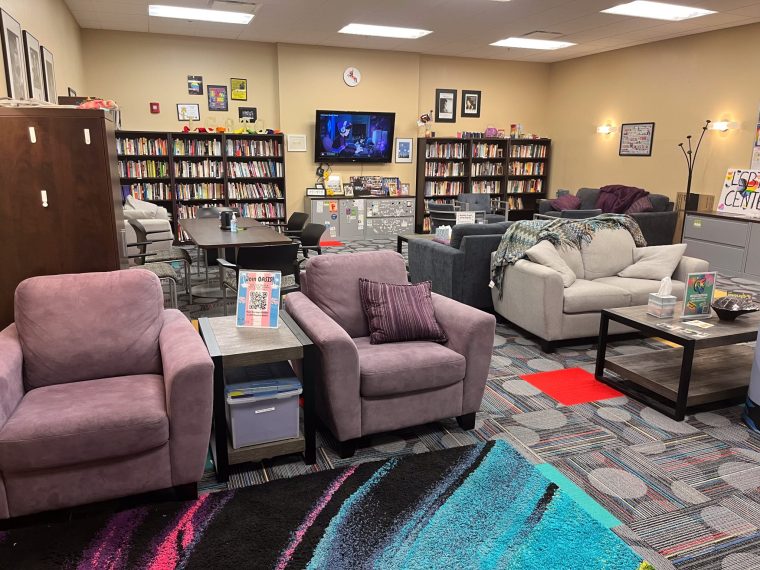Photos of the LGBTQ Resource Center displays full bookshelf, large cushioned seats and bright color carpet.