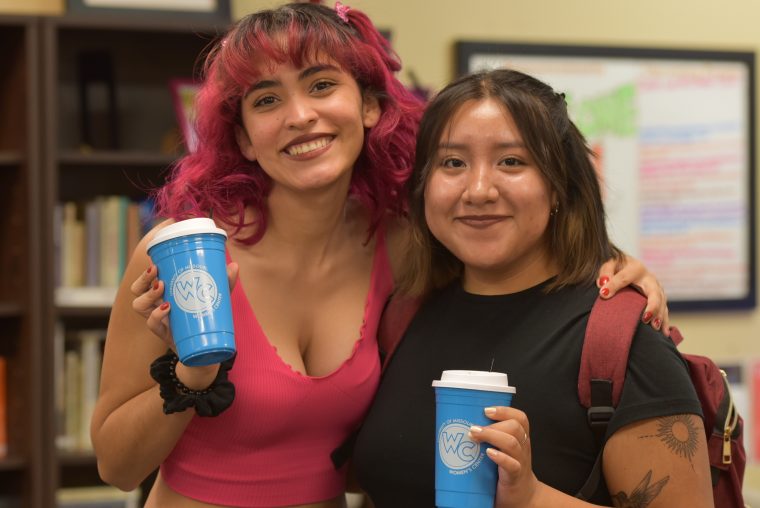 Two students smile for photo in Women's Center holding blue Women's Center cups.