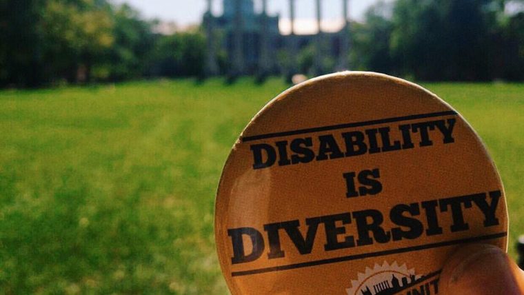 Disability is Diversity button is held up on the Quad with the Columns and Jesse Hall in the background
