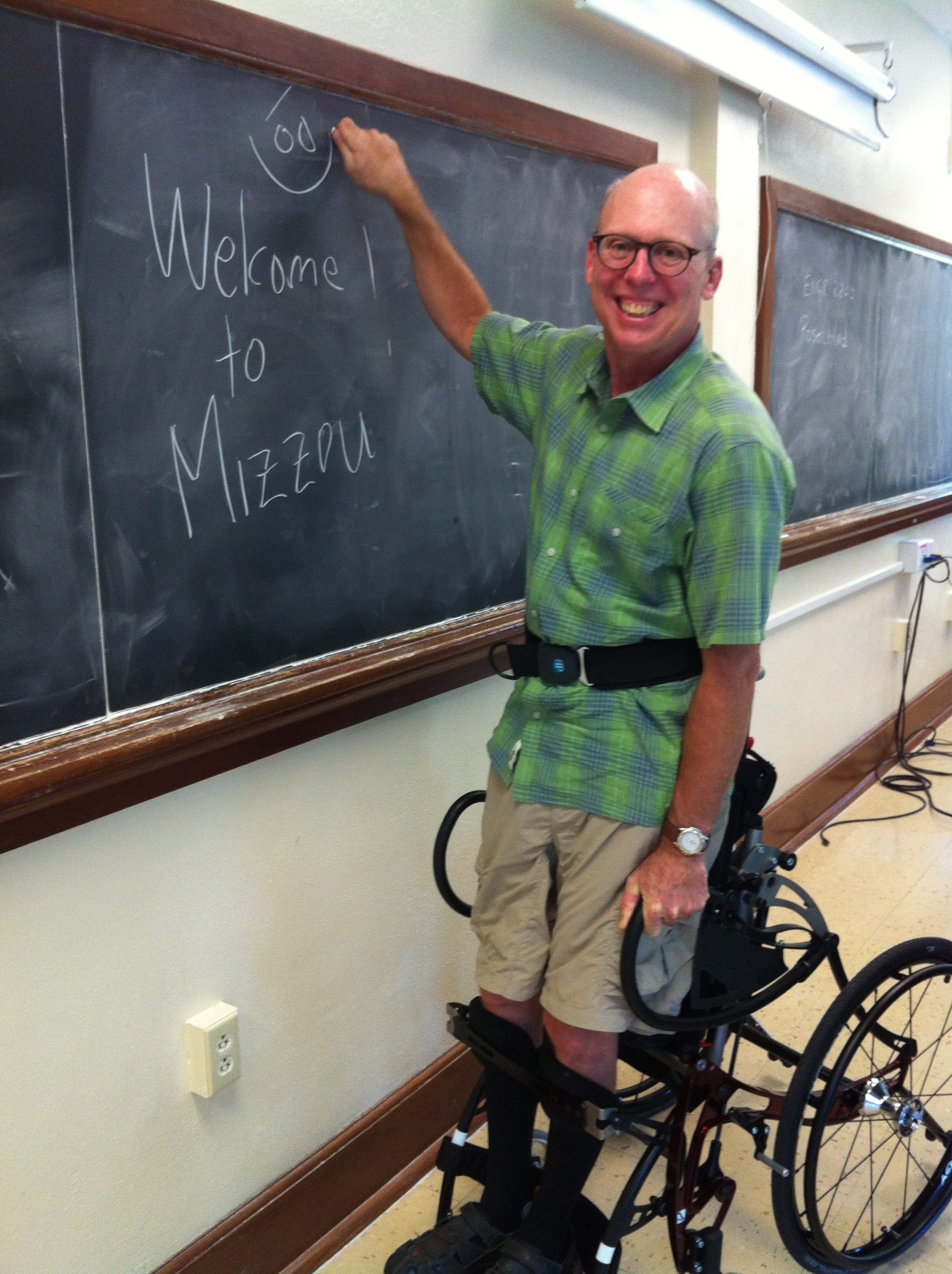 Professor using accessible device stands at the front of the classroom