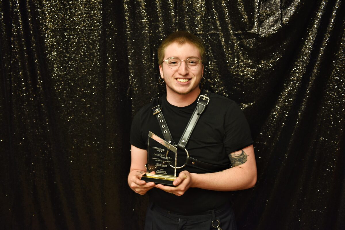 Student holding his Catalyst Award in a black outfit