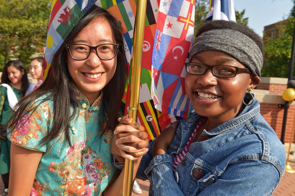Two girls holding world flags with hands interlocked around the pole.