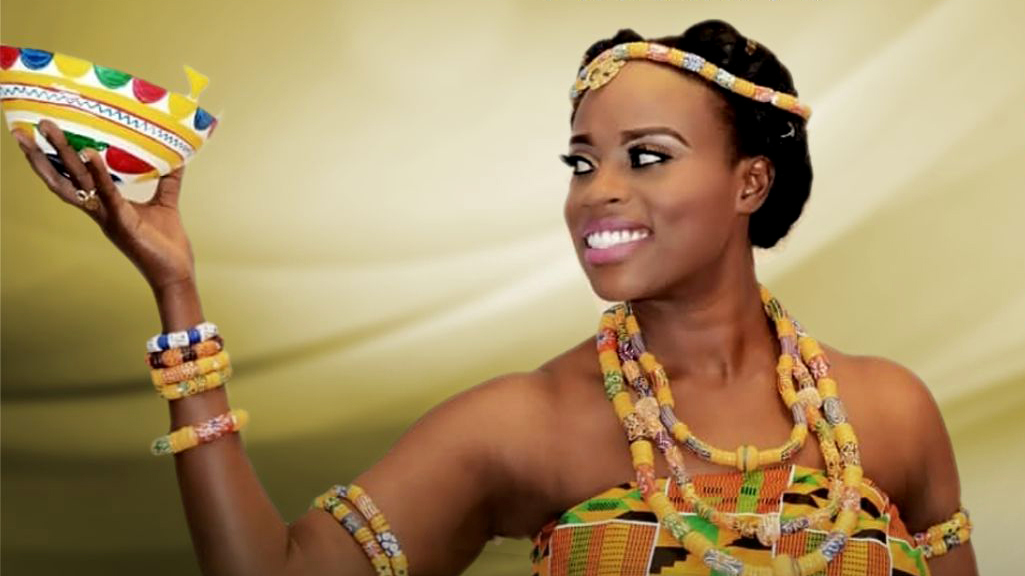 Woman in traditional African garb looking to the side while holding a bowl. Gold background.